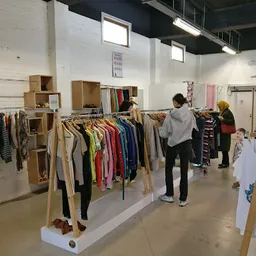 Winkelvloer met houten kledingrekken vol tweedehands kleding, enkele bezoekers aan het winkelen