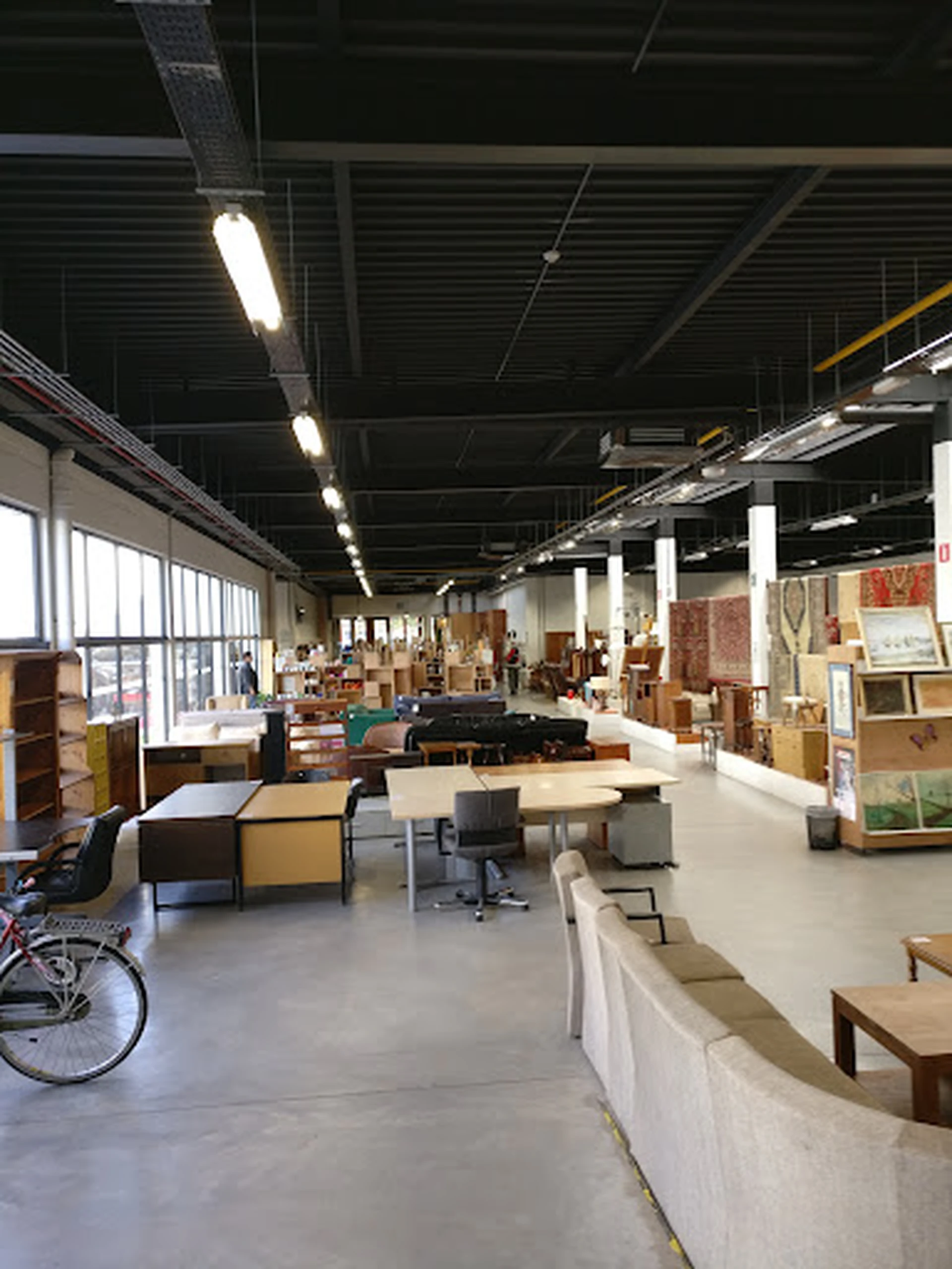 Ruim winkelinterieur met werkafdelingen, stellingen, meubels en verschillende goederen verspreid over de vloer