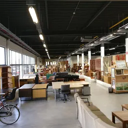 Ruim winkelinterieur met werkafdelingen, stellingen, meubels en verschillende goederen verspreid over de vloer