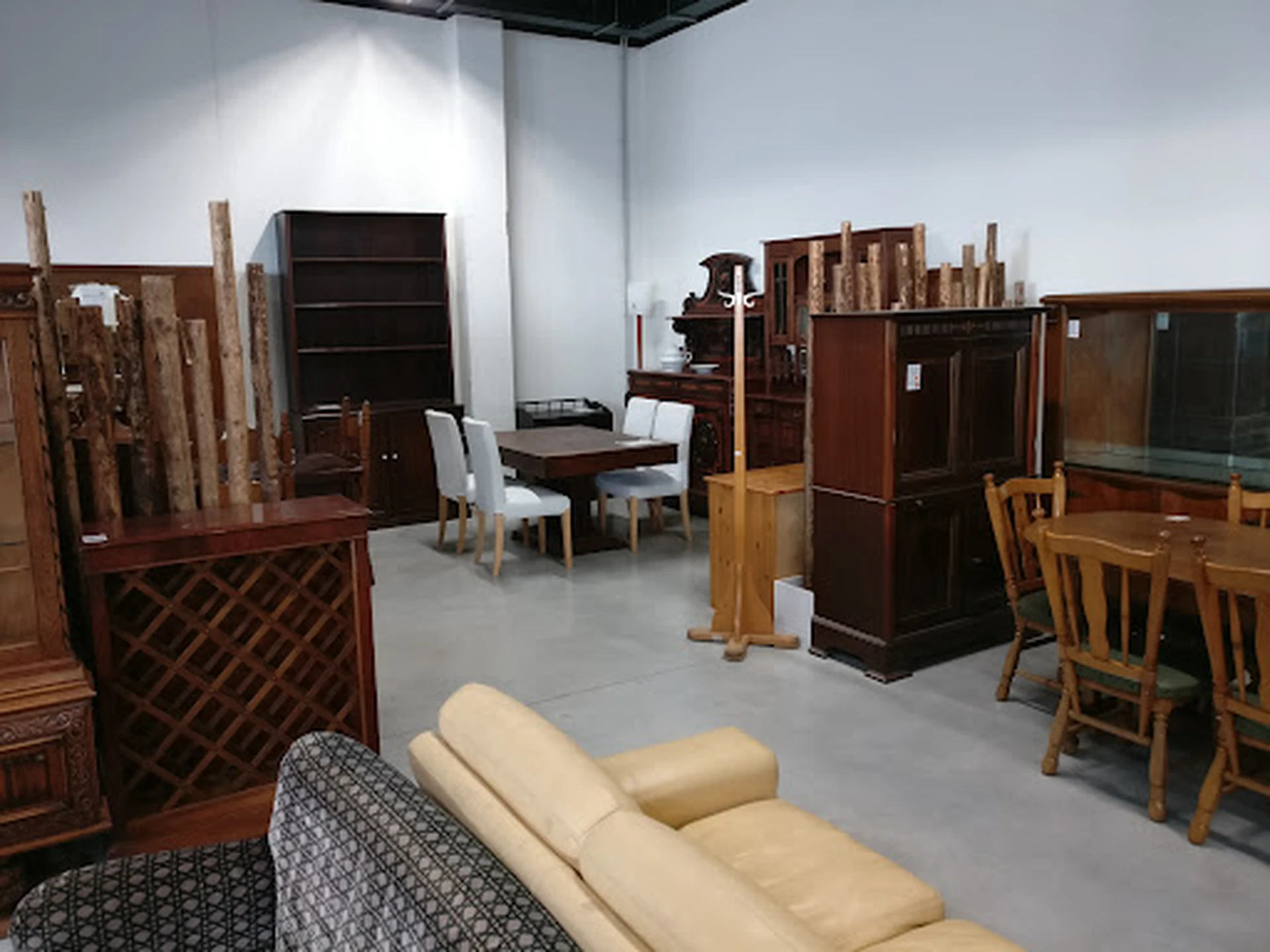 Winkelvloer met verschillende meubels: houten tafels, stoelen, kasten en een beige bank op voorgrond