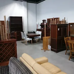 Winkelvloer met verschillende meubels: houten tafels, stoelen, kasten en een beige bank op voorgrond