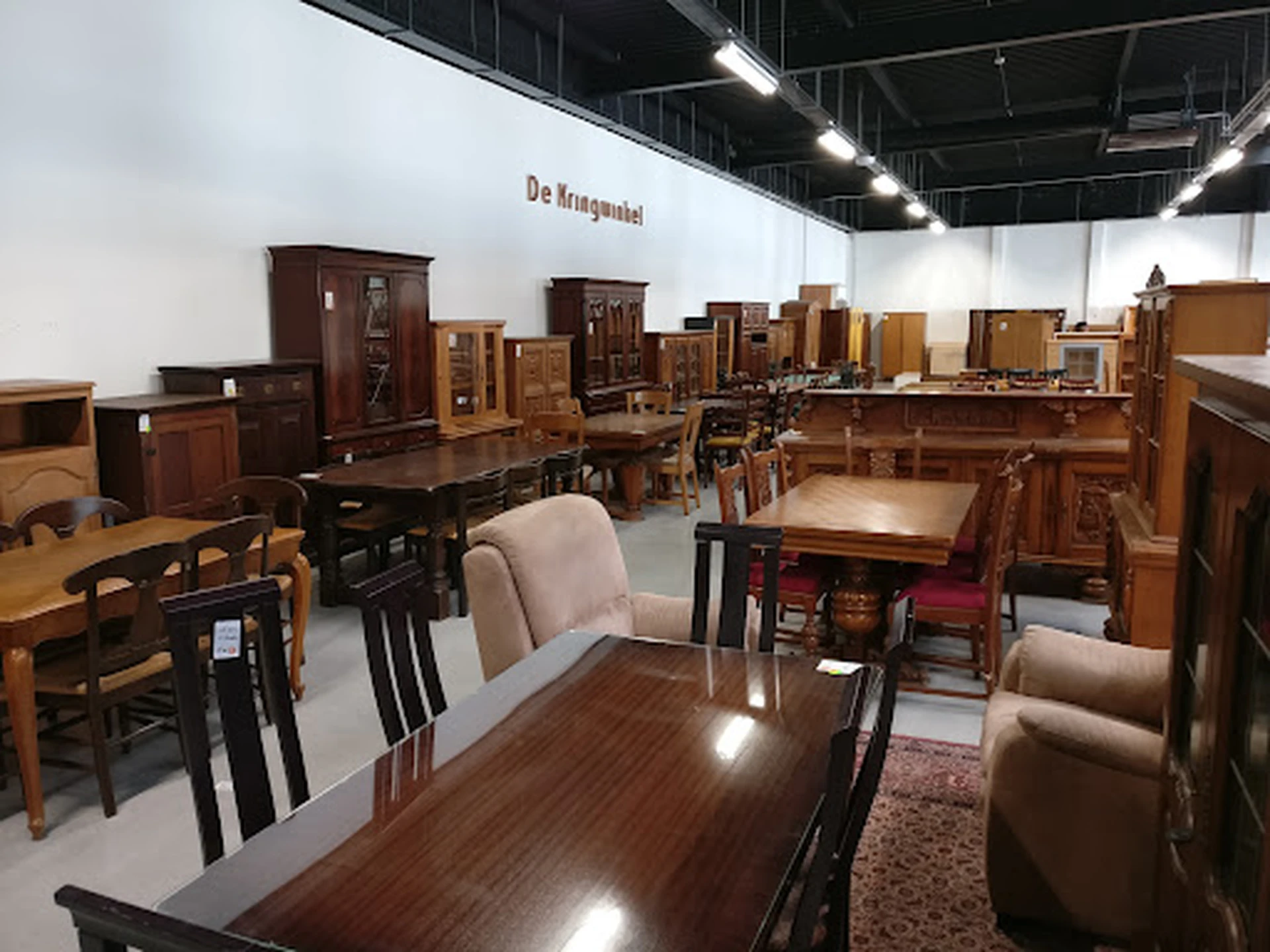 Uitgestalde houten meubelen in een kringloopwinkel, waaronder tafels, kasten, stoelen en andere huisraad