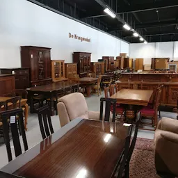 Uitgestalde houten meubelen in een kringloopwinkel, waaronder tafels, kasten, stoelen en andere huisraad