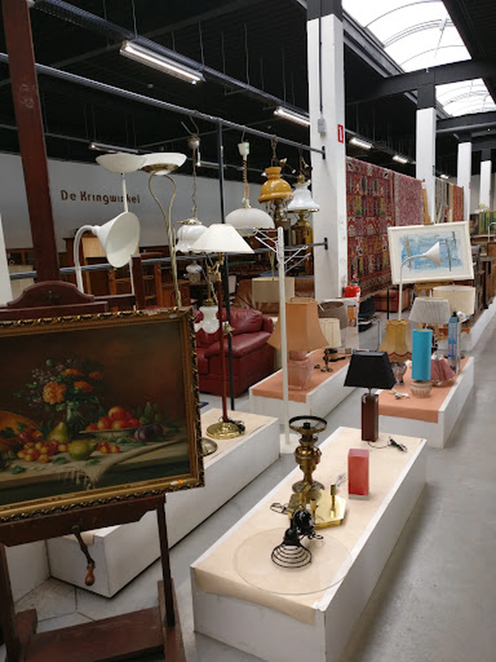 Vitrinekast met diverse tweedehands huishoudartikelen: lampen, vazen, sieraden en decoratieve objecten op witte display-blokk