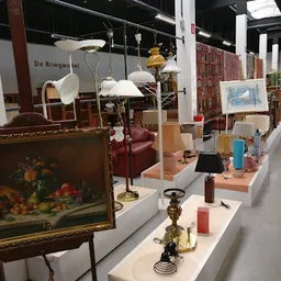 Vitrinekast met diverse tweedehands huishoudartikelen: lampen, vazen, sieraden en decoratieve objecten op witte display-blokk