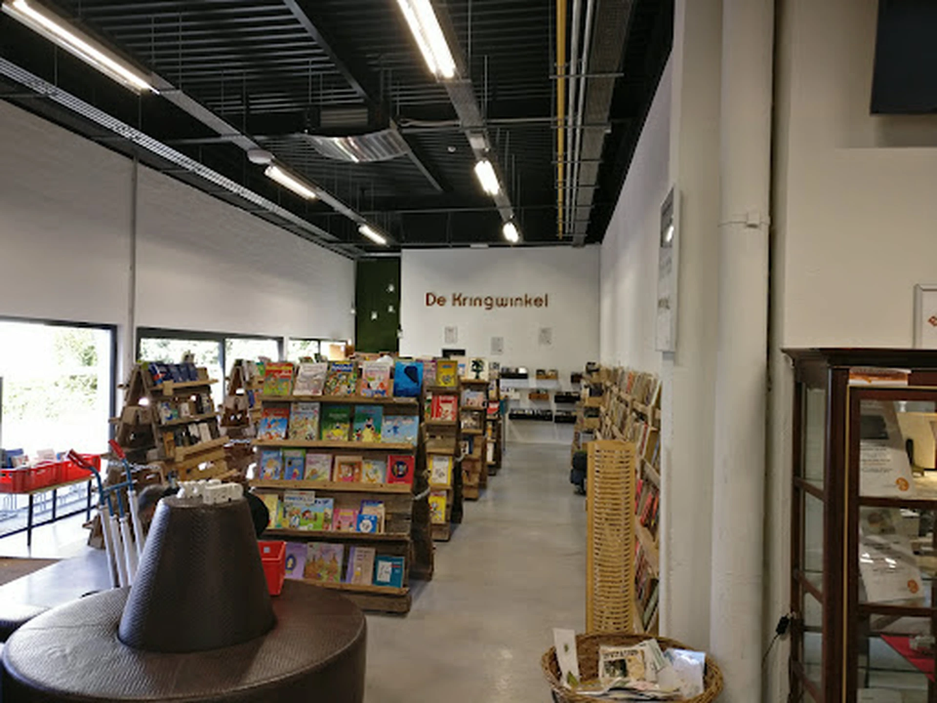 Winkelinterieur met boekenrekken en spullen uitgestald, naam 'De Kringwinkel' zichtbaar op muur