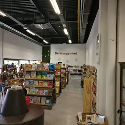 Winkelinterieur met boekenrekken en spullen uitgestald, naam 'De Kringwinkel' zichtbaar op muur