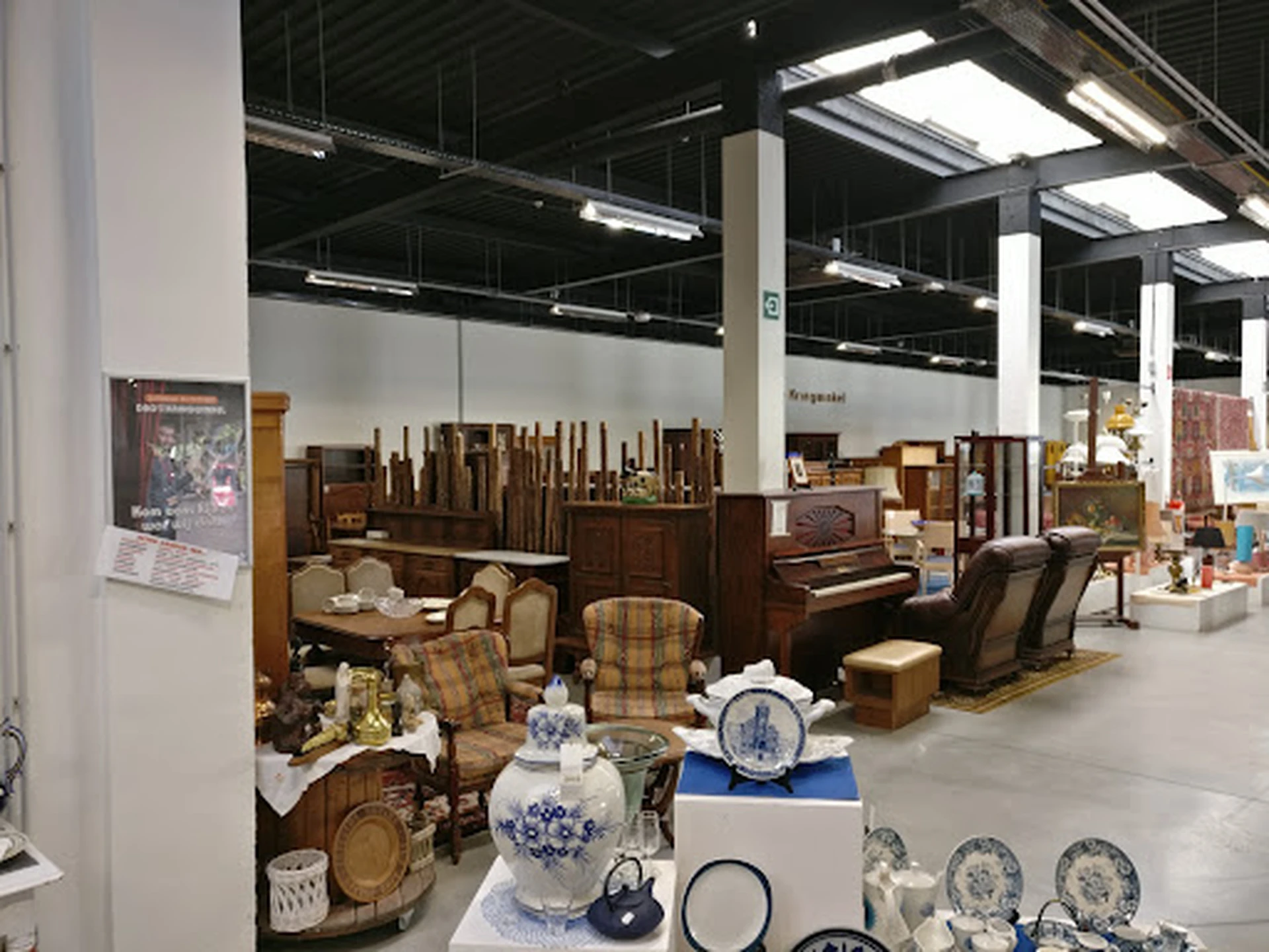 Uitgestalde meubels en decoratiestukken in een kringloopwinkel, waaronder stoelen, tafels, servies en lampen