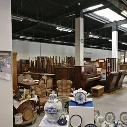 Uitgestalde meubels en decoratiestukken in een kringloopwinkel, waaronder stoelen, tafels, servies en lampen