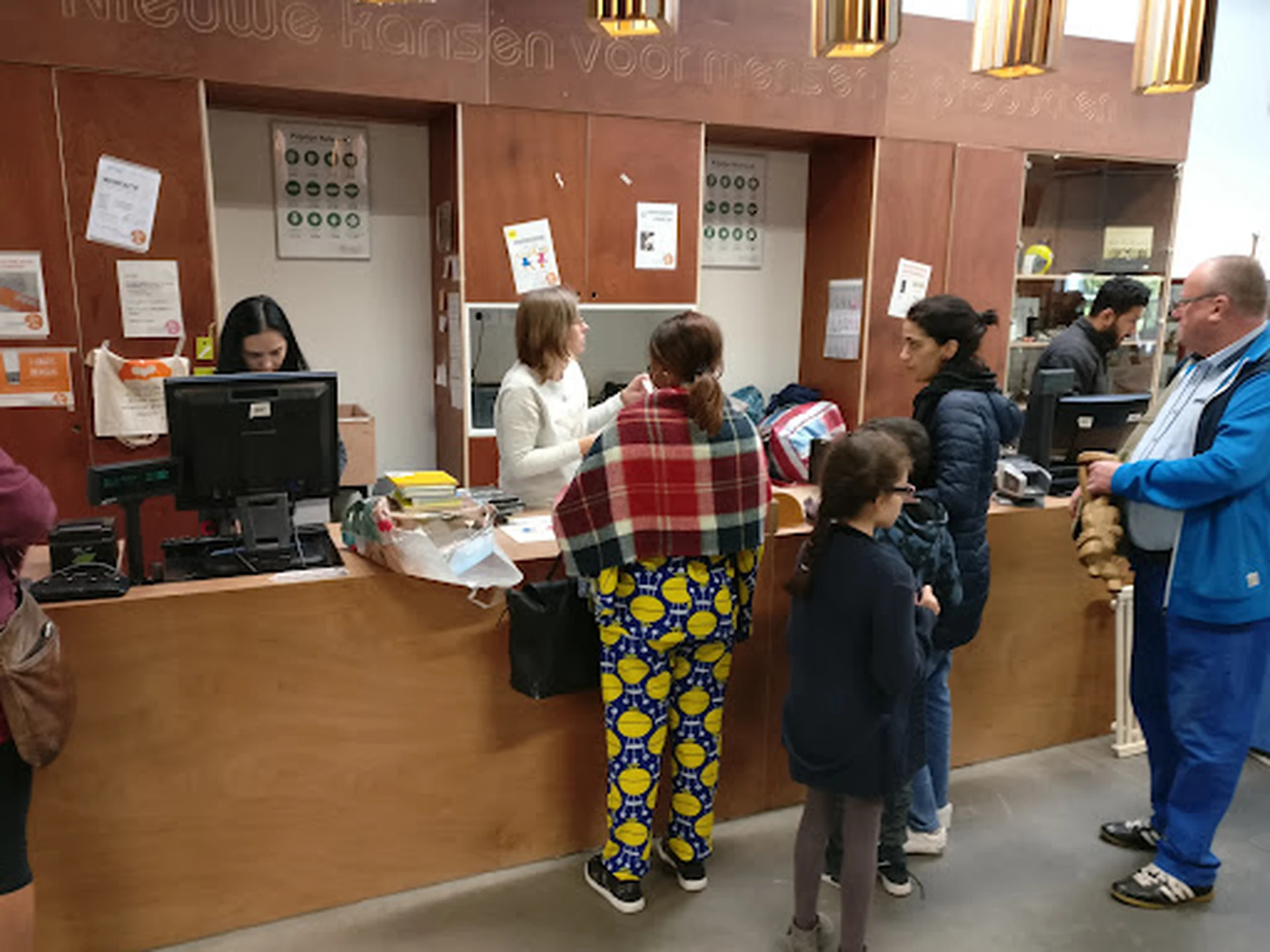 Bezoekers aan de balie van een kringloopwinkel, personeel helpt klanten