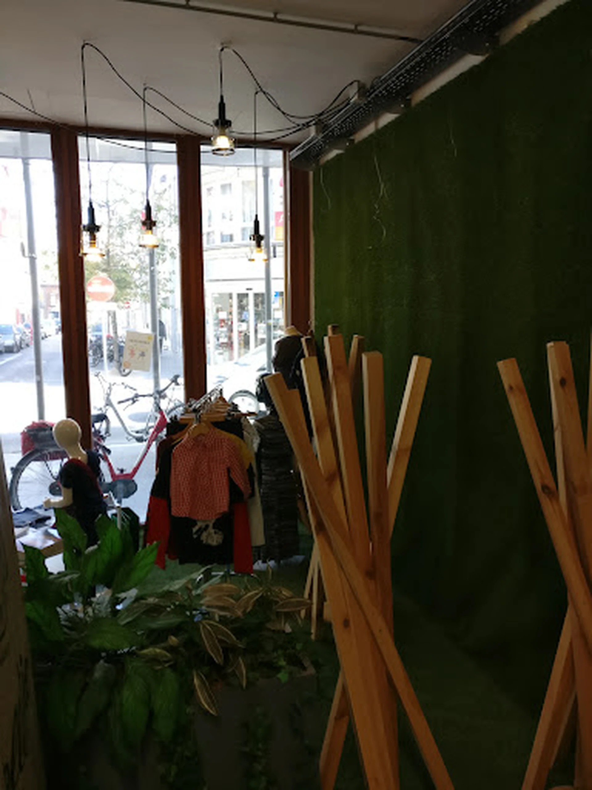 Winkelinterieur met kledingrek, houten stoelen tegen groene muur, raam met uitzicht op straat