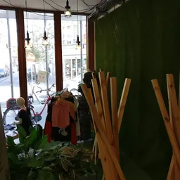 Winkelinterieur met kledingrek, houten stoelen tegen groene muur, raam met uitzicht op straat