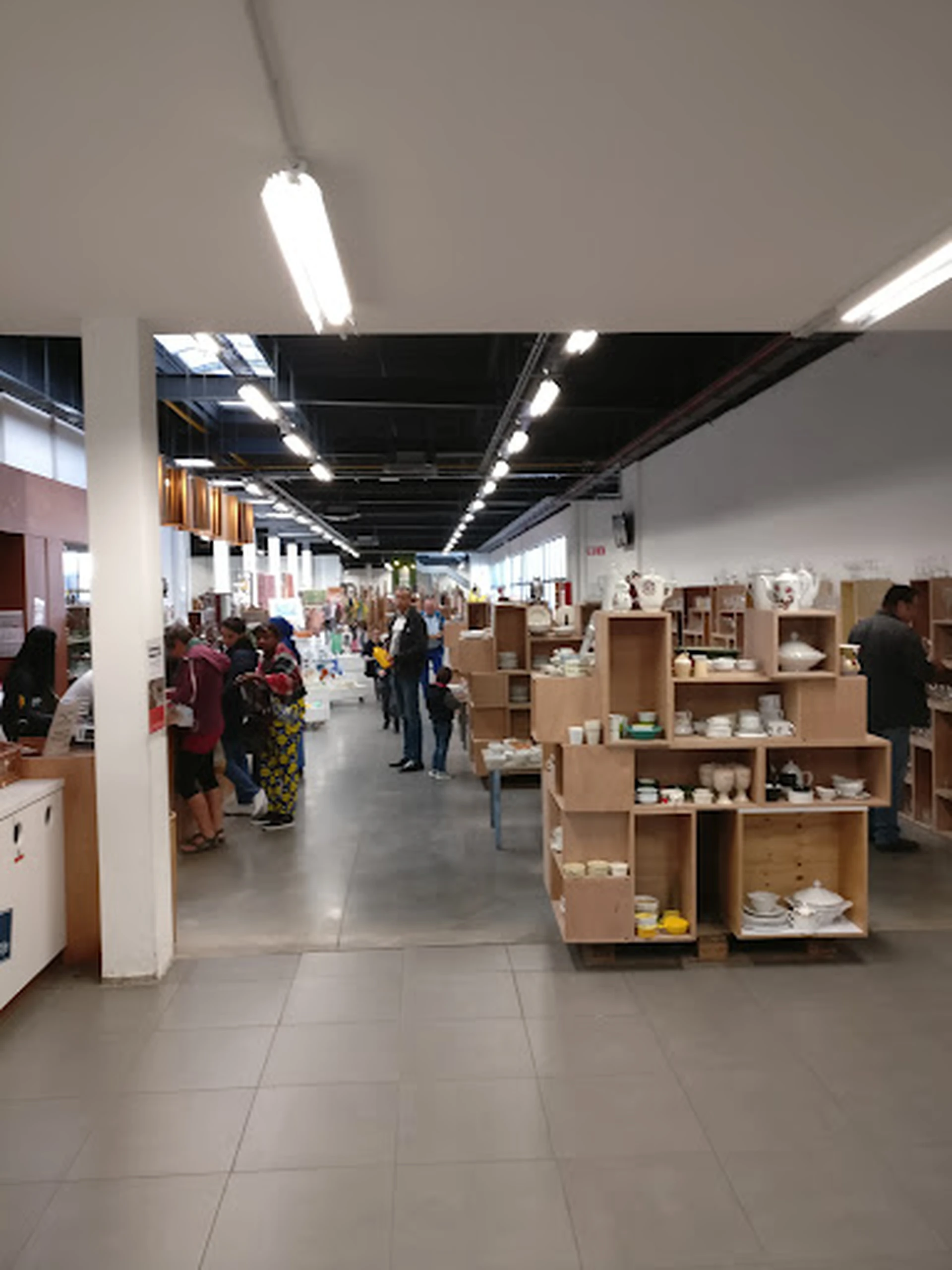 Ruime winkelhal met houten stellingen vol serviesgoed, bezoekers tussen de rekken