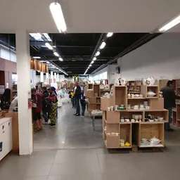 Ruime winkelhal met houten stellingen vol serviesgoed, bezoekers tussen de rekken