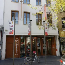 Witte gevel van kringloopwinkel met bruine deuren en ramen op begane grond, winkelnaam zichtbaar