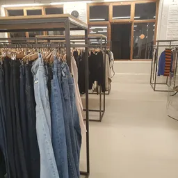 Rekken met tweedehands kleding, vooral jassen en jeans op hangers in de winkel