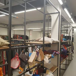 Winkelinterieur met metalen stellingen vol kleding, beddenspullen en diverse tweedehands artikelen