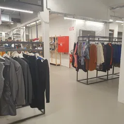 Winkelinterieur met kledingrekken vol tweedehands kleding, verlichte plafonds en witte muren