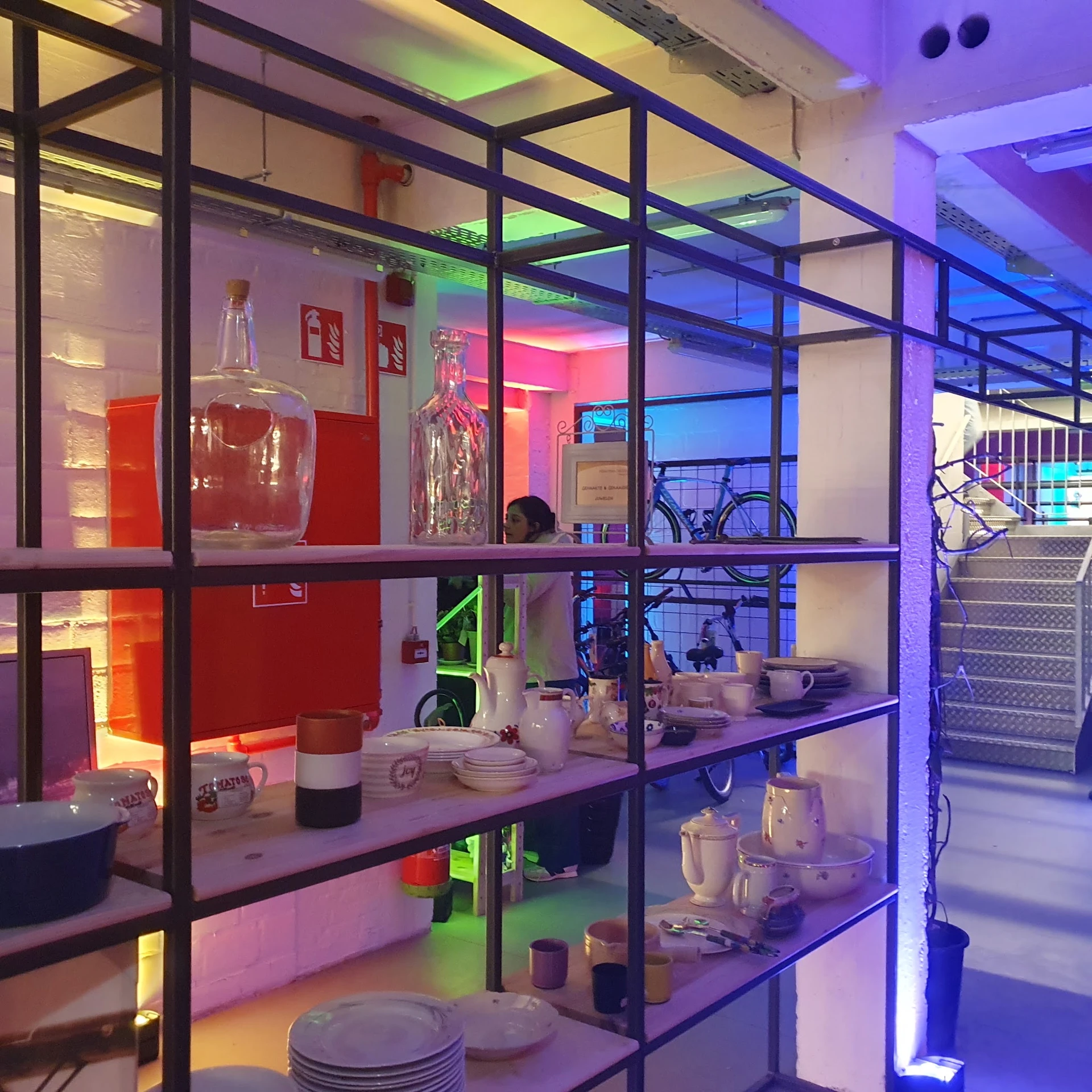 Vitrinekasten met huishoudelijke artikelen zoals servies, pannen en keukenapparatuur onder kleurig neonlicht
