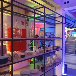 Vitrinekasten met huishoudelijke artikelen zoals servies, pannen en keukenapparatuur onder kleurig neonlicht