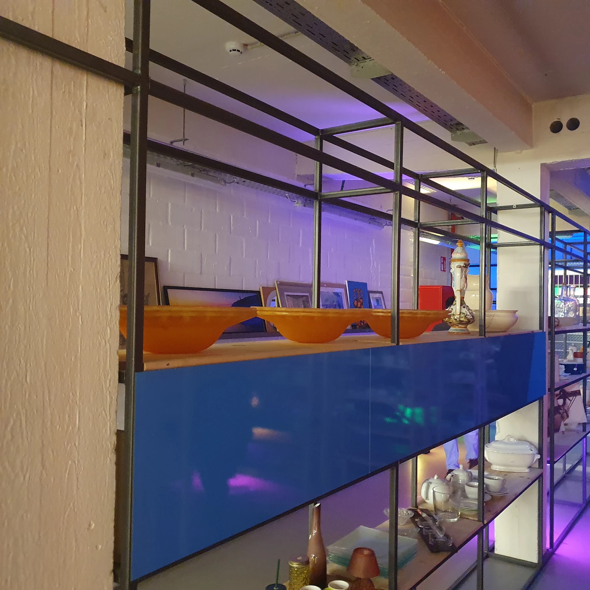 Glazen afscheiding in winkelinterieur met oranje en blauwe elementen, verlicht met paars licht