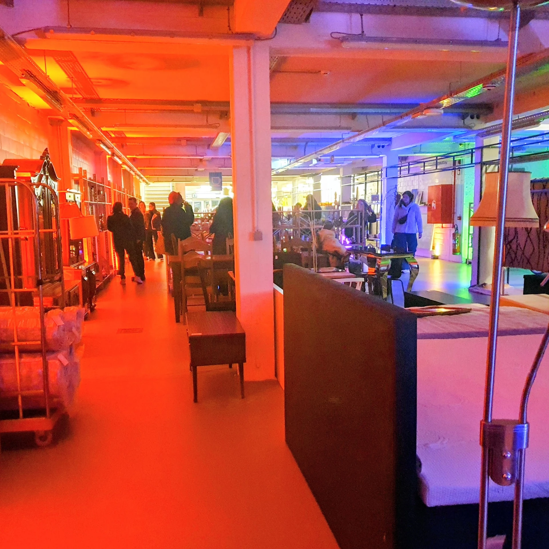 Winkelvloer met kleurrijke neonverlichting in rood, blauw en groen; stellingen met kleding en diverse spullen langs de zijkan