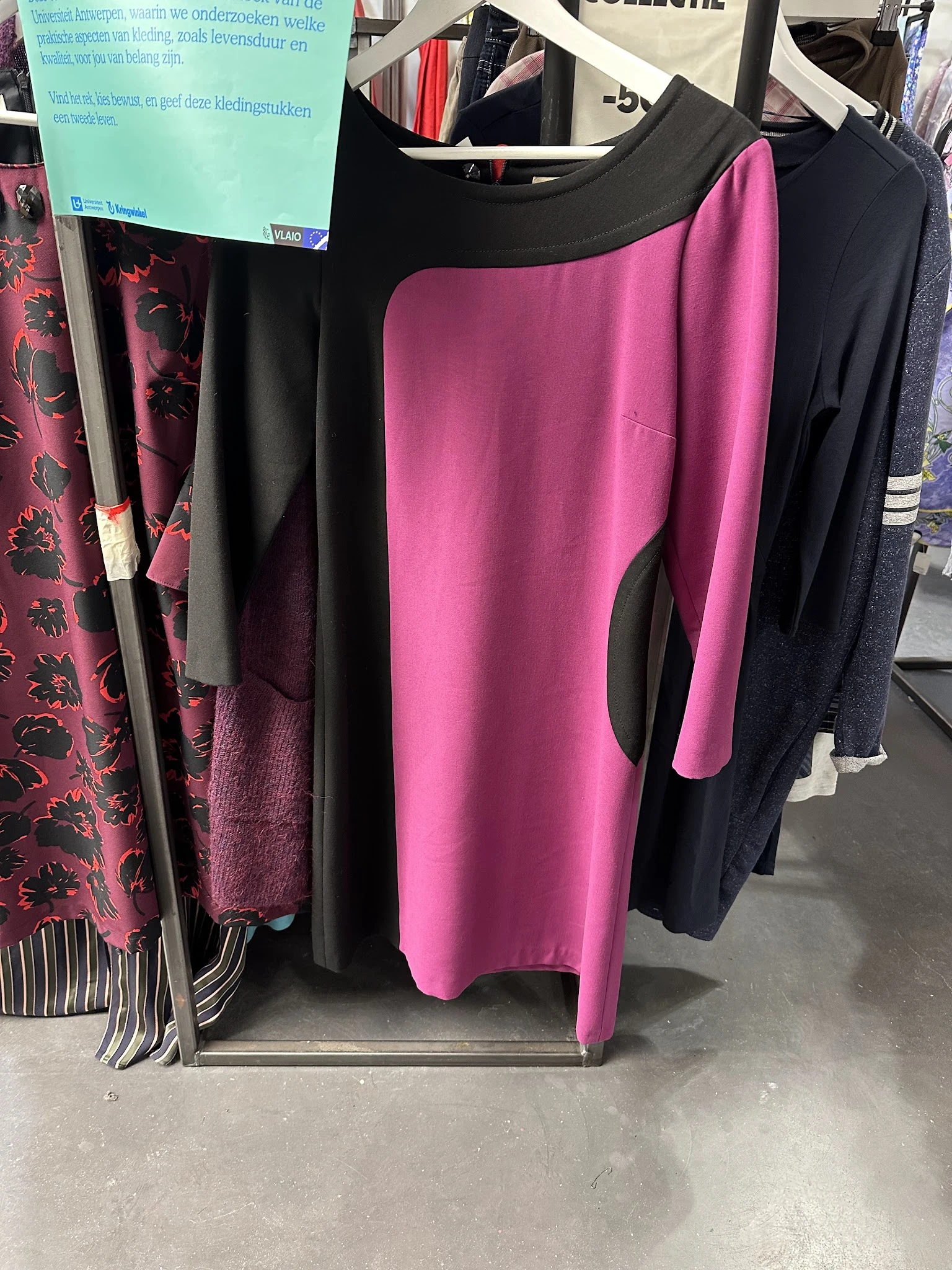 Rekken met tweedehands dameskleding in verschillende kleuren, waaronder roze, zwart en paarse kledingstukken