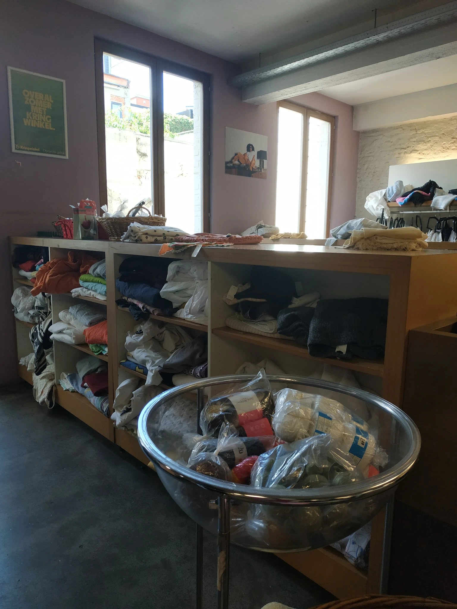 Houten kastmeubel met open vakken vol met tweedehands kleding en textiel in verschillende kleuren