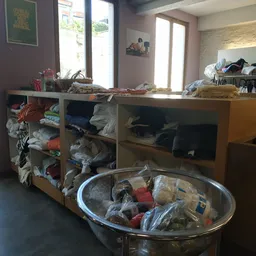 Houten kastmeubel met open vakken vol met tweedehands kleding en textiel in verschillende kleuren