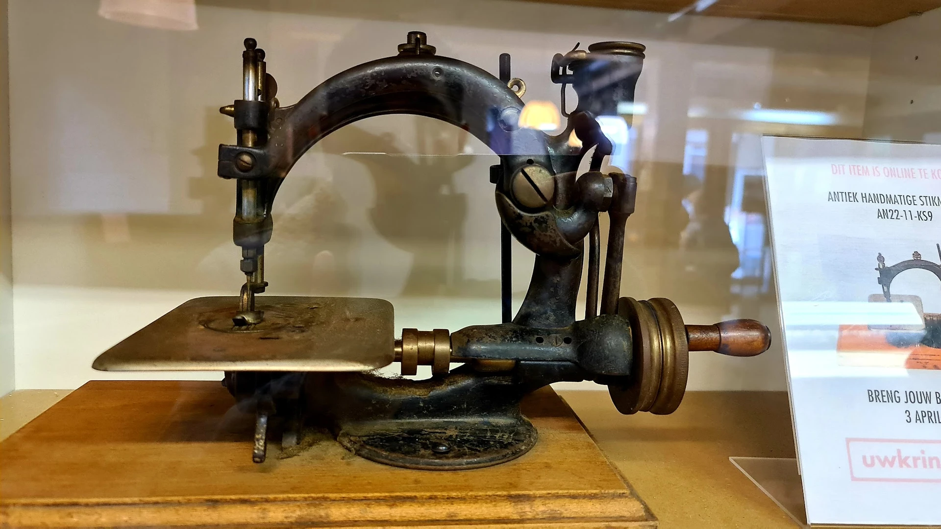 Antieke naaimachine met zwart gietijzer frame en houten handvat, tentoongesteld in vitrine