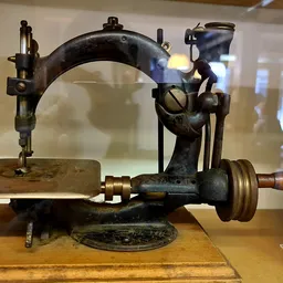 Antieke naaimachine met zwart gietijzer frame en houten handvat, tentoongesteld in vitrine