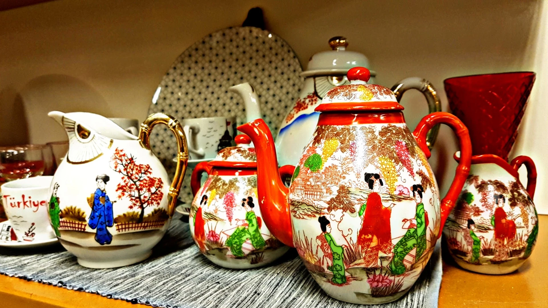 Decoratieve Aziatische theepot en melkkan met rode handvaten en kleurrijke taferelen, op display met porselein