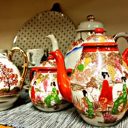 Decoratieve Aziatische theepot en melkkan met rode handvaten en kleurrijke taferelen, op display met porselein