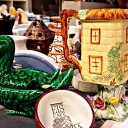 Verzameling decoratieve items op een tafel: groene eendenvaas, keramische huisjes, servies en andere vintage voorwerpen