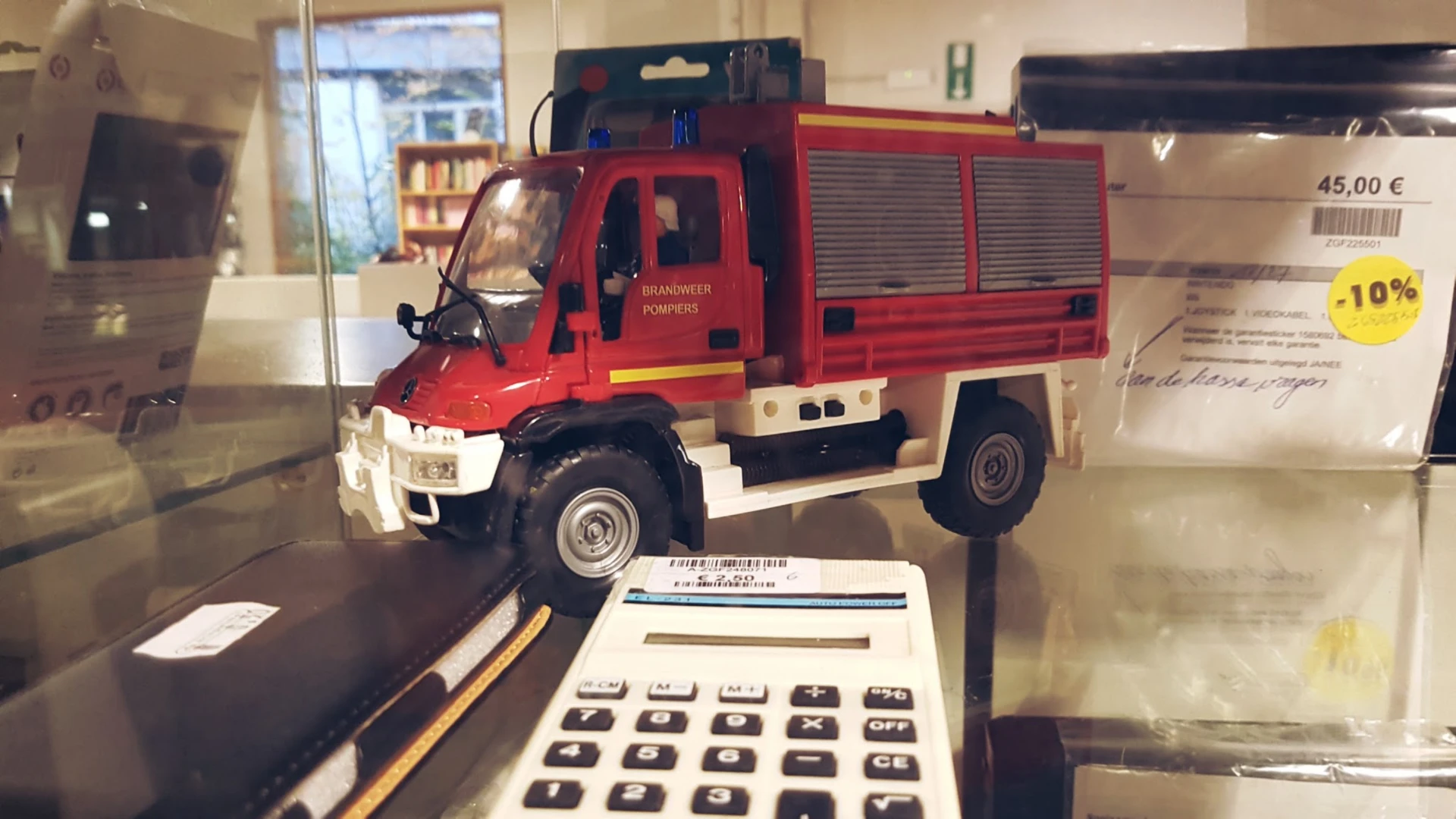 Miniatuurauto van een rode brandweerwagen in vitrine naast calculator