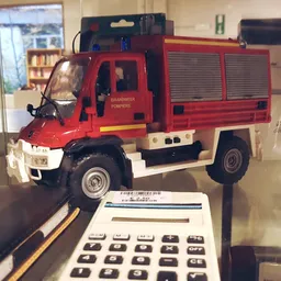 Miniatuurauto van een rode brandweerwagen in vitrine naast calculator
