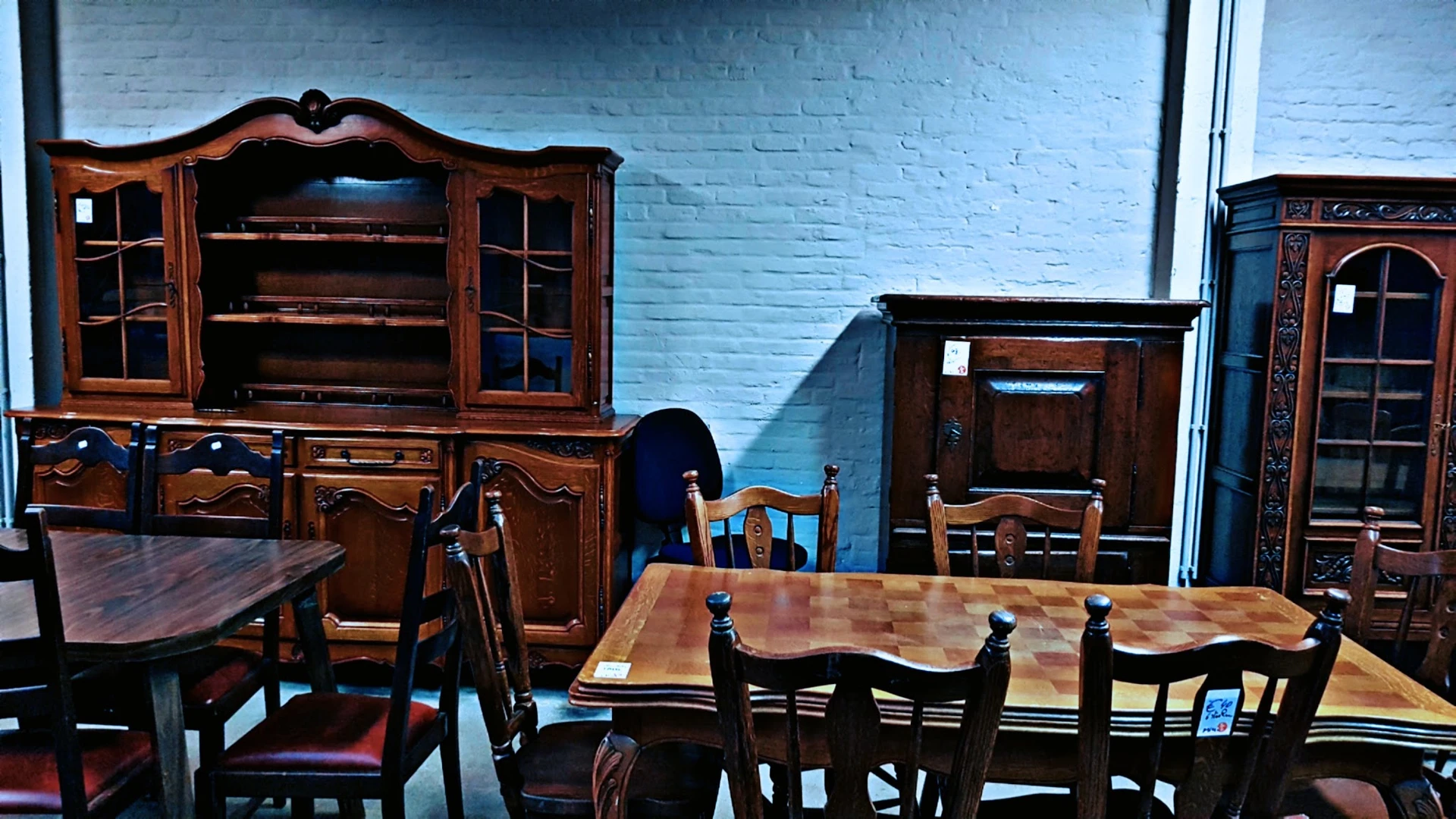 Tweedehands houten meubels uitgestald: antieke kasten, stoelen en tafels tegen blauwe muur