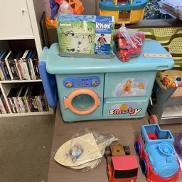 Speelgoedkeuken in turquoise met accessoires en boeken op achtergrond in kringloopwinkel