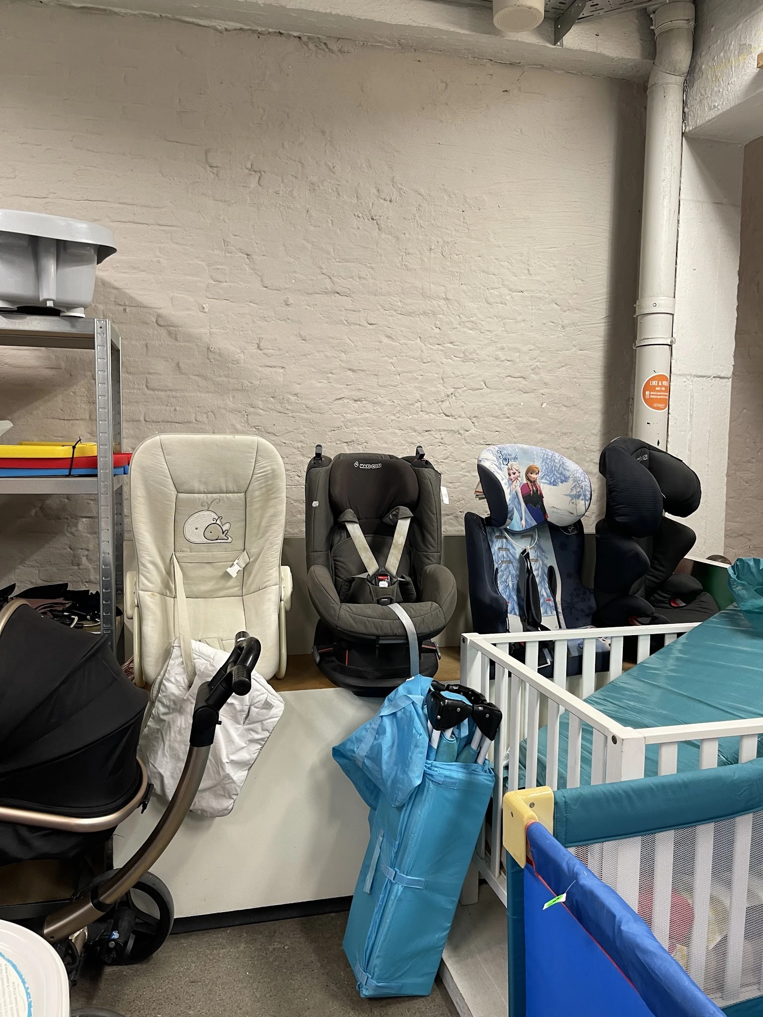 Verschillende tweedehands kinderstoelen en babyspeelgoed opgesteld tegen een muur in de winkel