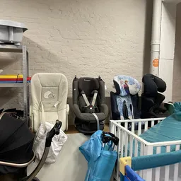 Verschillende tweedehands kinderstoelen en babyspeelgoed opgesteld tegen een muur in de winkel
