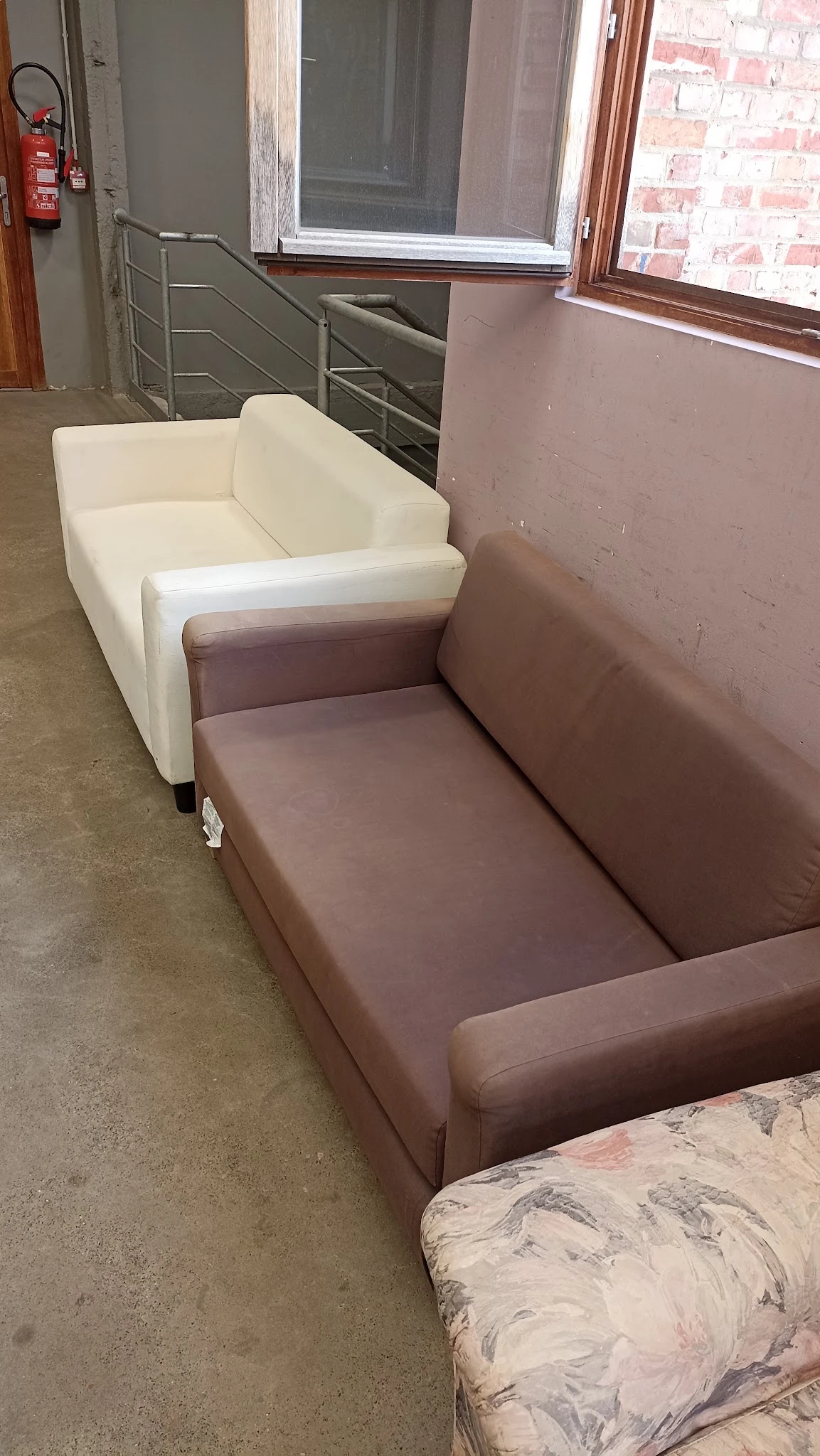 Twee meubels naast elkaar: een wit en een bruin/taupe gekleurde fauteuil of loungestoel op een betonnen vloer