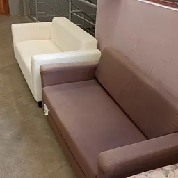 Twee meubels naast elkaar: een wit en een bruin/taupe gekleurde fauteuil of loungestoel op een betonnen vloer