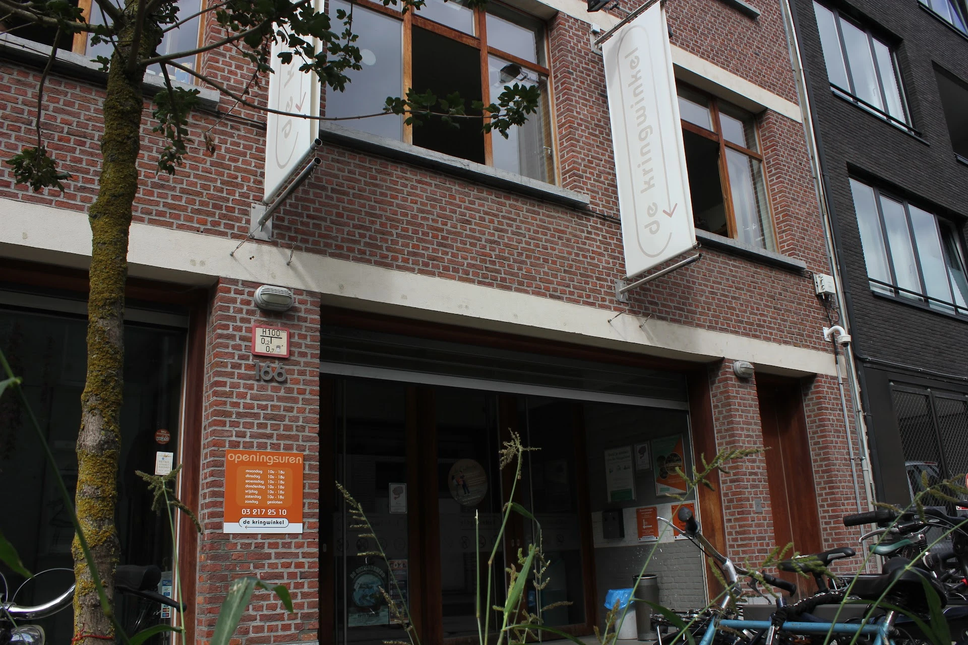 Gevel van kringloopwinkel met bakstenen muur, grote etalageruit en ingang op begane grond