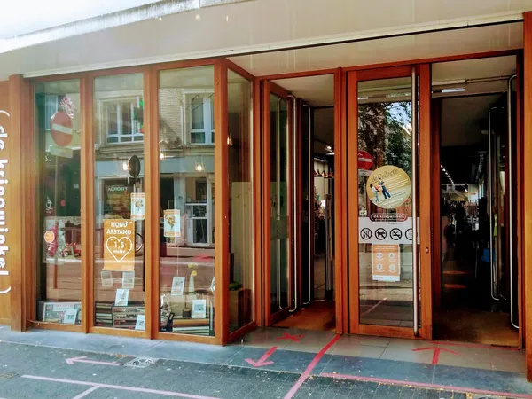 Winkelgevel met rode houten raamlijsten en glazen deuren, vitrine met spullen, ingang zichtbaar