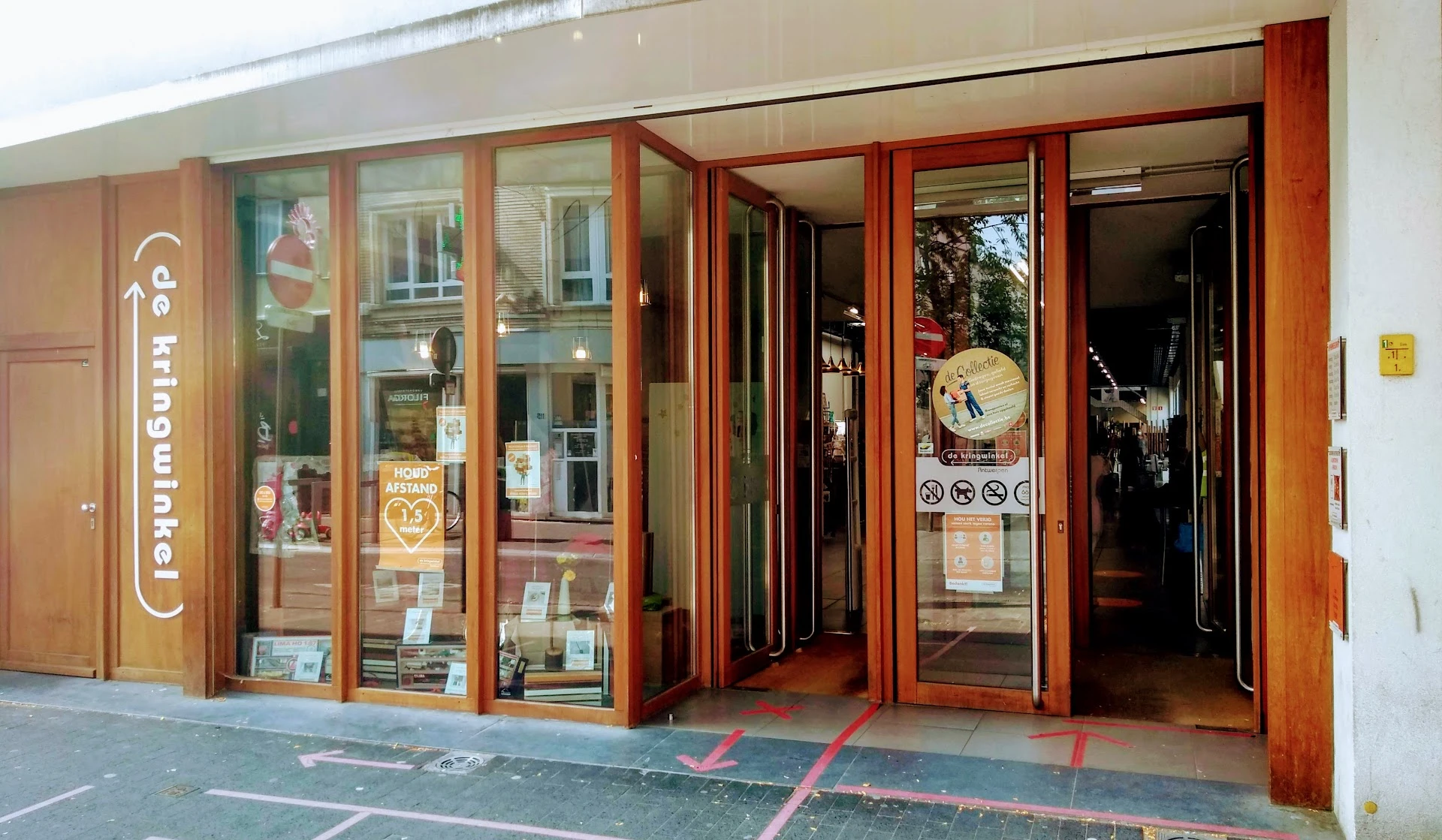 Winkelgevel met rode houten raamlijsten en glazen deuren, vitrine met spullen, ingang zichtbaar