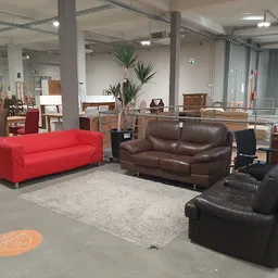 Winkelvloer met uitgestalde zitmeubels: rode bank, bruine leren bank en zwarte fauteuil op tapijt