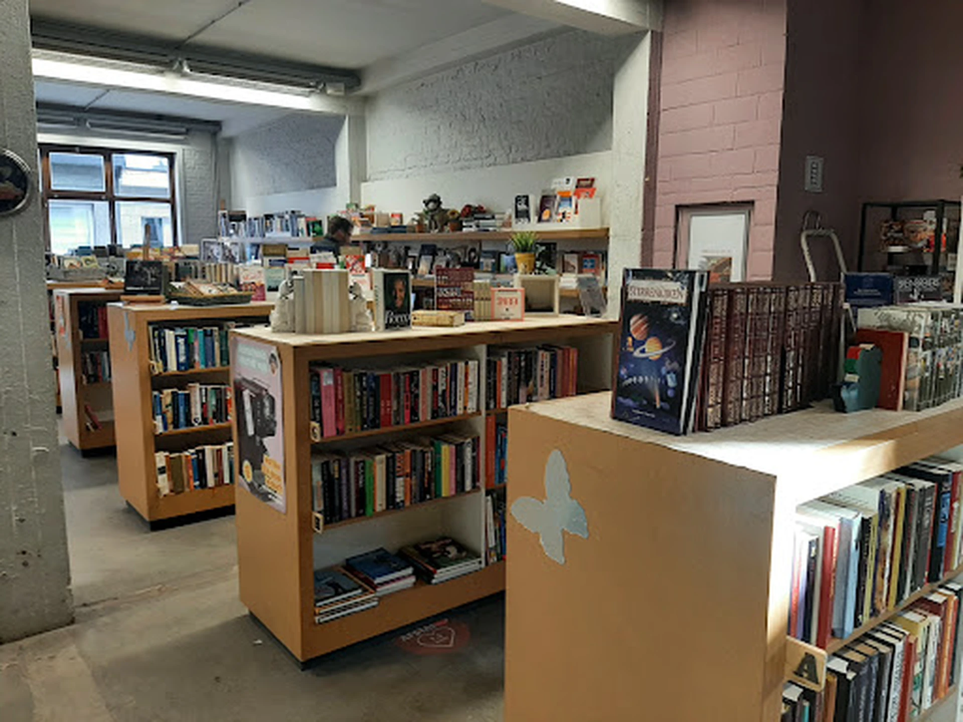 Binnenaanzicht van een kringloopwinkel met houten boekenkasten op wielen en boeken in verschillende stellingen