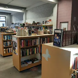 Binnenaanzicht van een kringloopwinkel met houten boekenkasten op wielen en boeken in verschillende stellingen