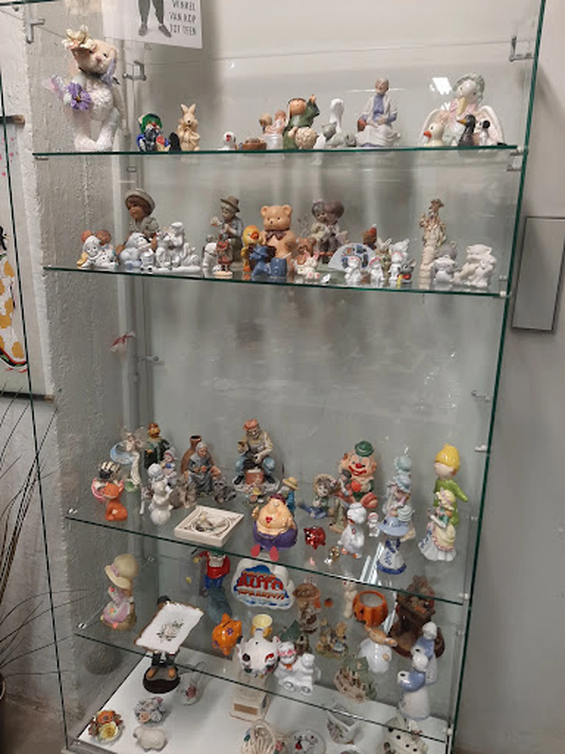 Glazen vitrinekast met verzameling decoratieve beeldjes, porseleinen figuren en verzamelaars items op meerdere planken