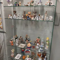 Glazen vitrinekast met verzameling decoratieve beeldjes, porseleinen figuren en verzamelaars items op meerdere planken